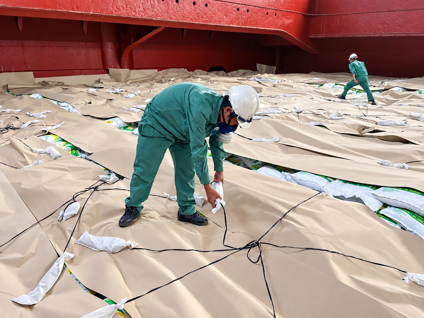 Personnel working on covered bagged cargo inside a vessel hold